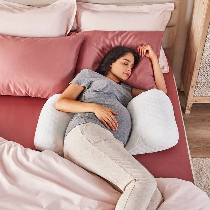 The model is lying on the white pillow placed on pink sheets on the bed.
