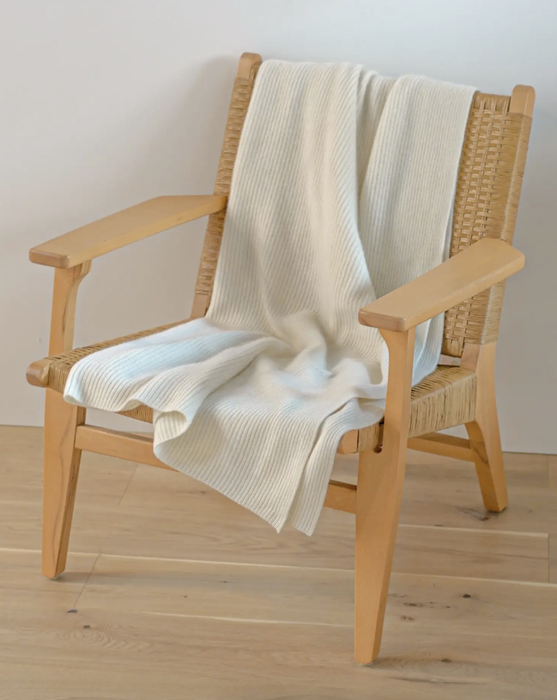 A cream-hued cashmere throw draped over a wooden armchair