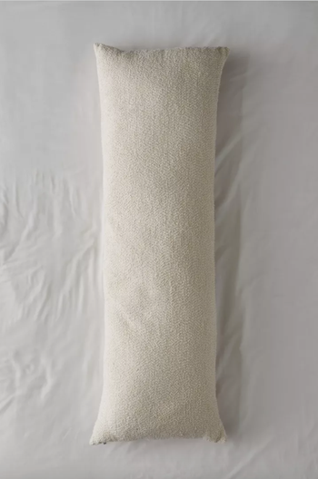 Image of the beige body pillow laid on pristine white sheets
