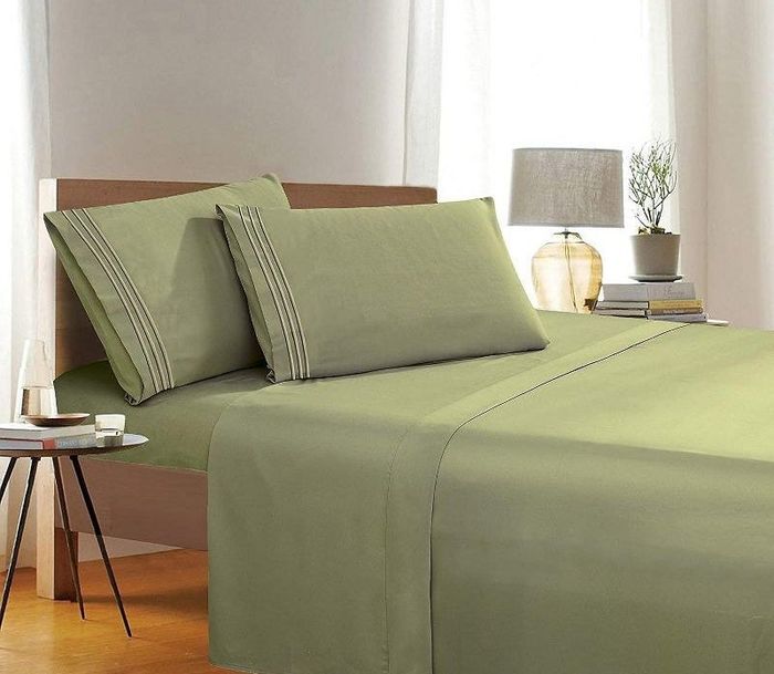 A beautifully staged bedroom with green sheets on a neatly made bed, accompanied by two bedside tables, one featuring a lamp on top.