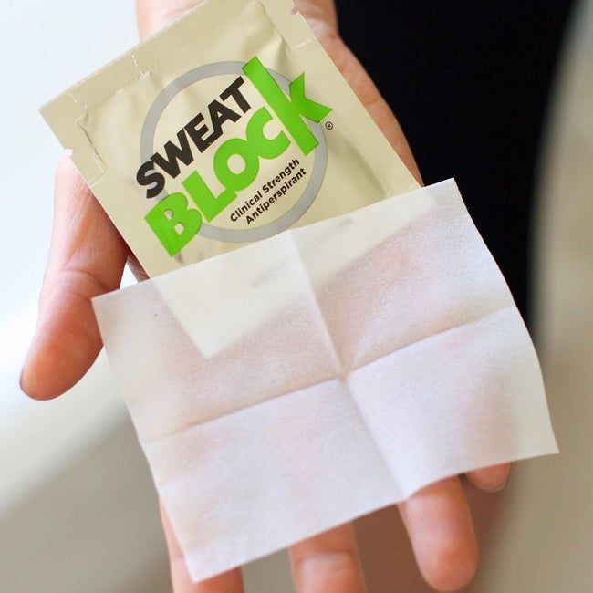A hand holding a package of SweatBlock wipes