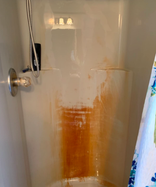 A photo showing the condition of a rusty shower wall before cleaning.