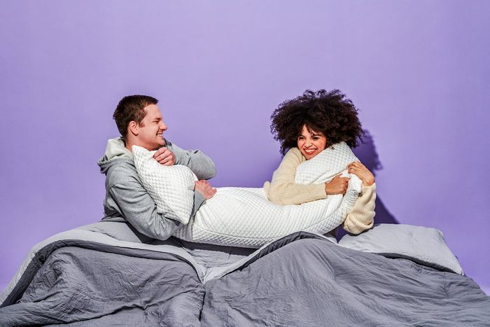 Two models snuggling with the white body pillow while lying in bed