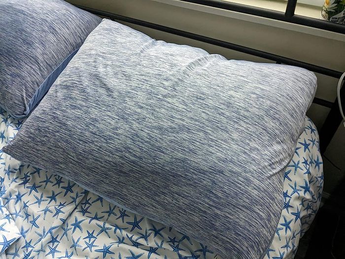 The blue-gray cooling pillowcases resting on pillows on a reviewer's bed