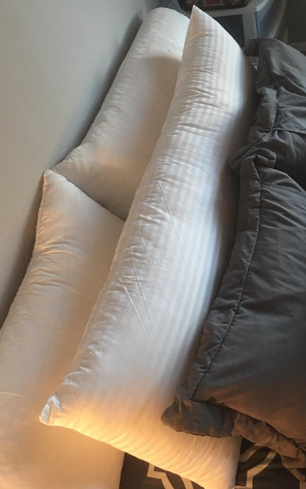 A photo from a reviewer showcasing the white pillow on their bed alongside other pillows