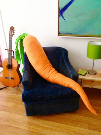 Image of the carrot-shaped pillow resting on a blue chair