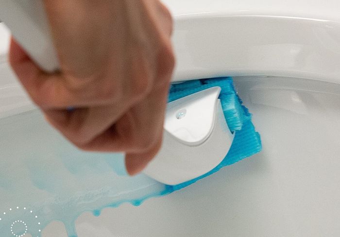 A person using the cleaning kit to scrub the toilet.