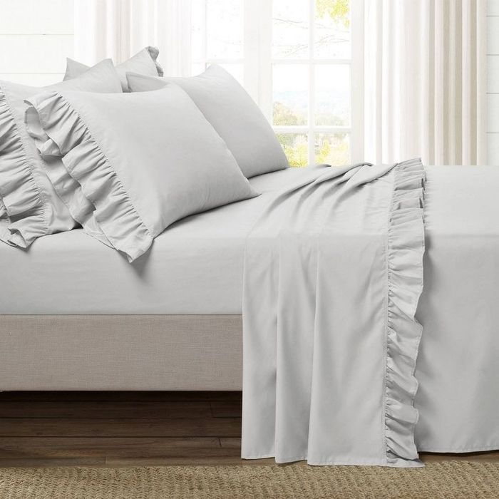 Grey bedding with delicate ruffled edges arranged on a bed.