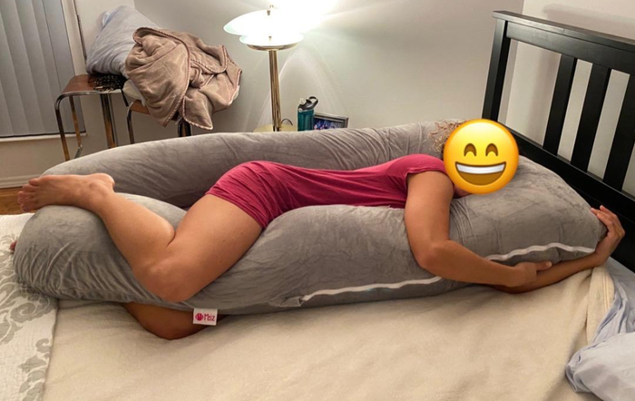 Reviewer lying on a light gray U-shaped pregnancy pillow