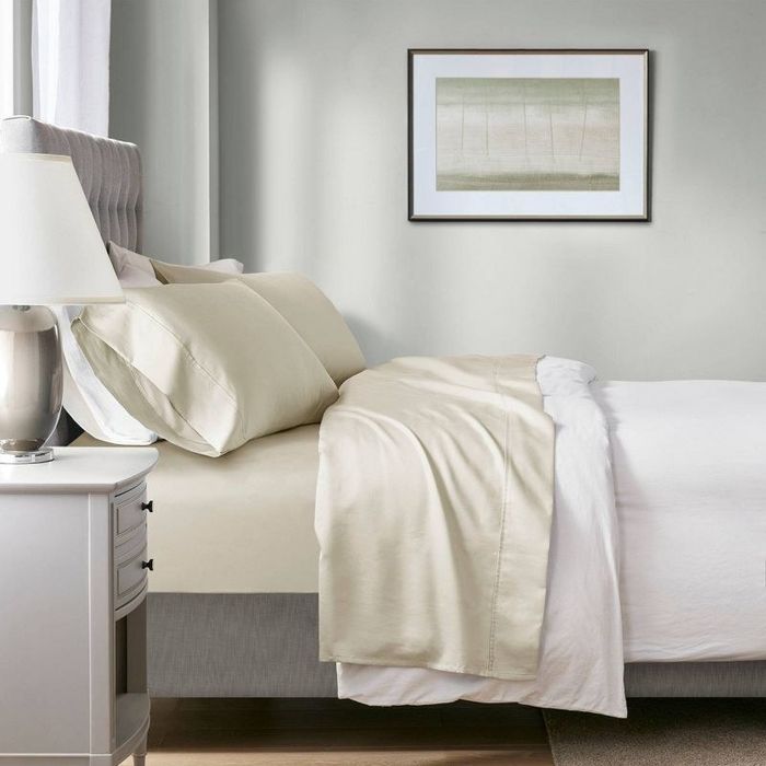 A neatly made bed with cream-colored sheets in a beautifully staged bedroom, featuring a bedside table and artwork hanging on the wall.