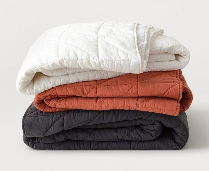 A stack of quilts in white, orange, and black hues.