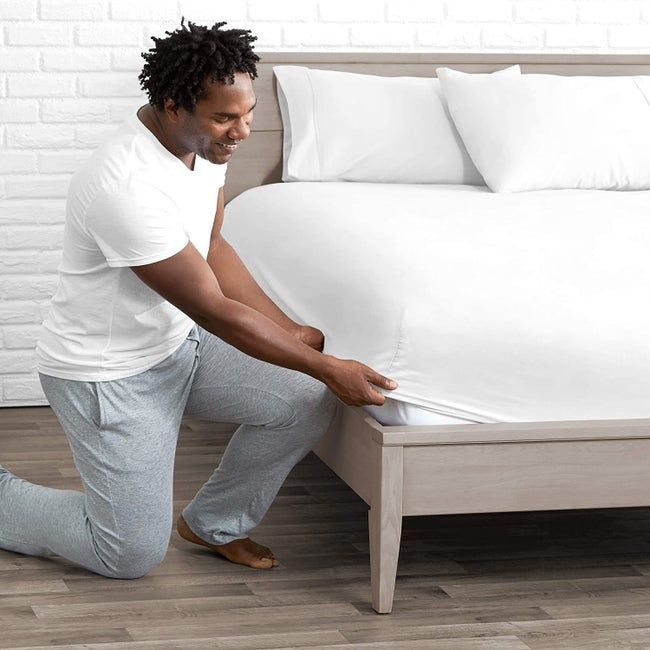A model in their pajamas adjusting a white fitted sheet over the mattress