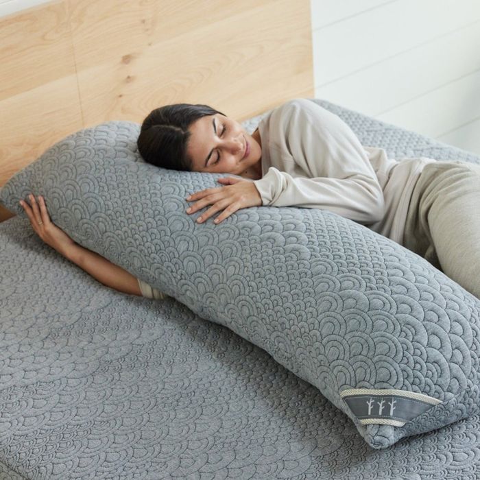 Model lying beside the body pillow on a bed
