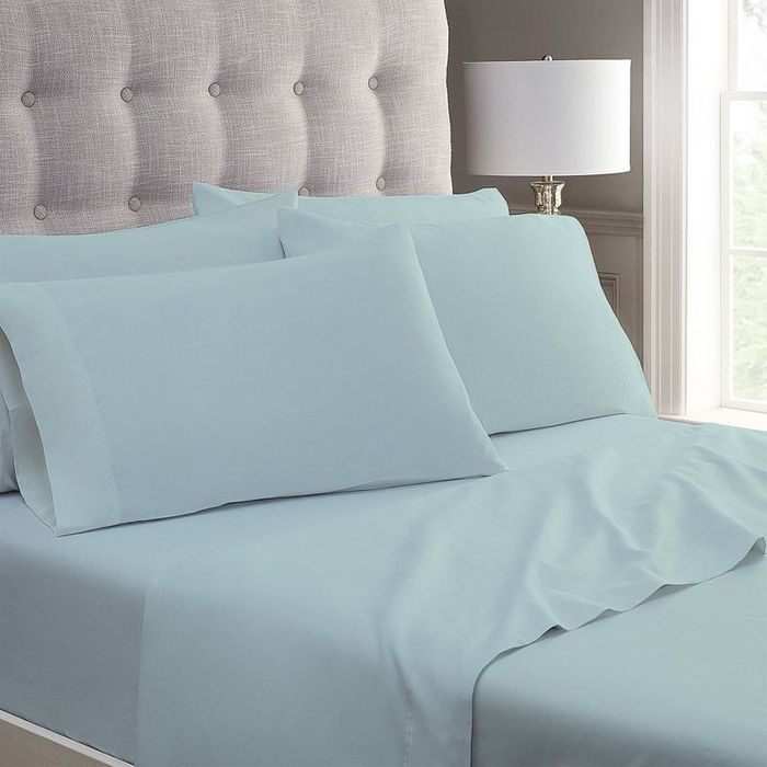 A neatly made bed featuring a plush headboard with blue folded sheets arranged perfectly.