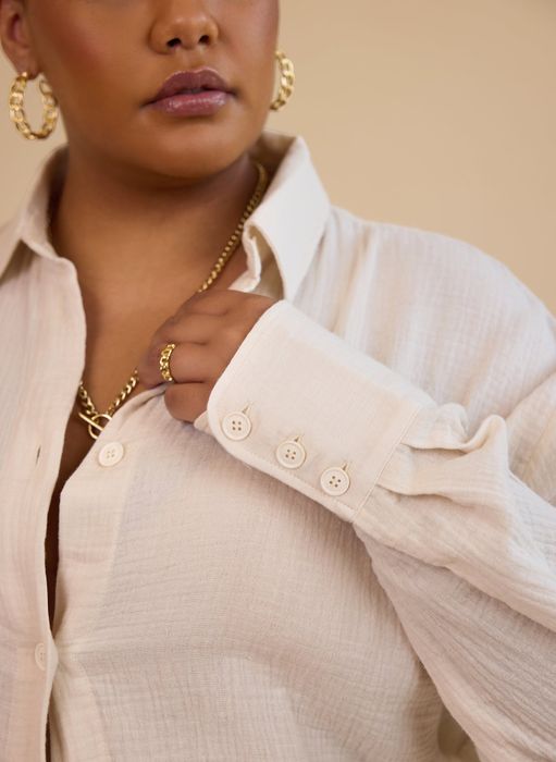 A person wearing hoop earrings and a gold necklace, paired with a button-up shirt crafted from textured fabric.