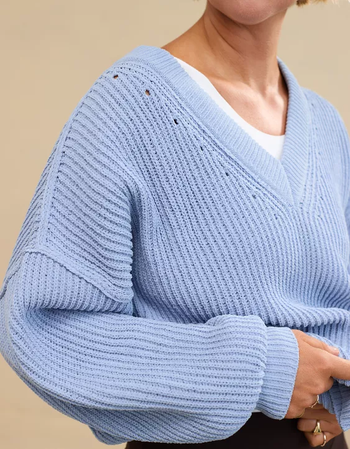 Person wearing a loose-knit V-neck sweater layered over a white top, showcasing a laid-back, casual vibe