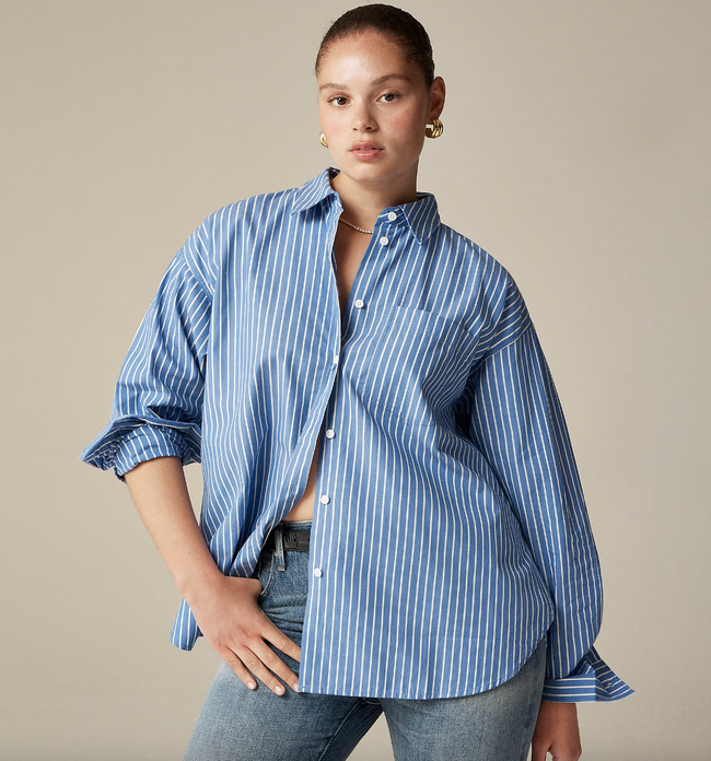 A model styled in a large blue and white striped button-up shirt paired with blue jeans, striking a pose with one hand in their pocket.