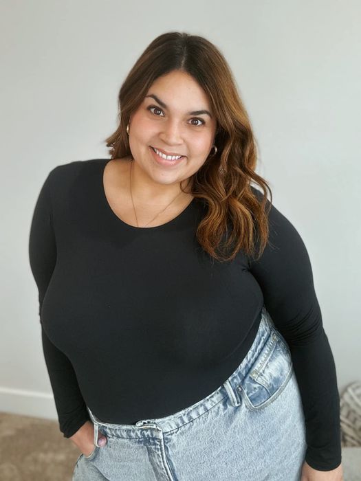 A reviewer flashes a smile while rocking a long-sleeve black top tucked into a pair of high-waisted jeans.