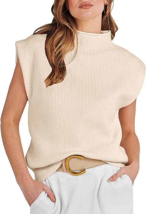 Model styling a sleeveless, high-neck ribbed top paired with white pants and a beige belt with a gold clasp.