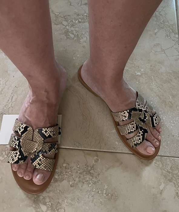 A reviewer models the shoes, featuring straps with a trendy snakeskin print.