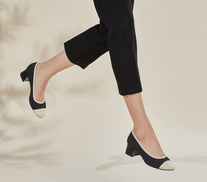A model is pictured wearing black shoes with a cream-colored toe cap.
