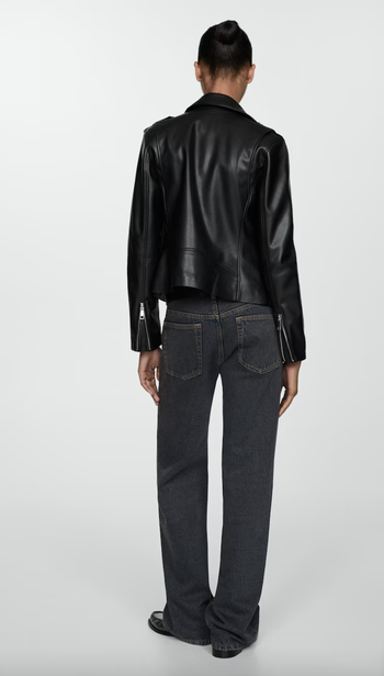 A model is striking a pose from the back, showing off a black leather jacket and dark wide-leg jeans.