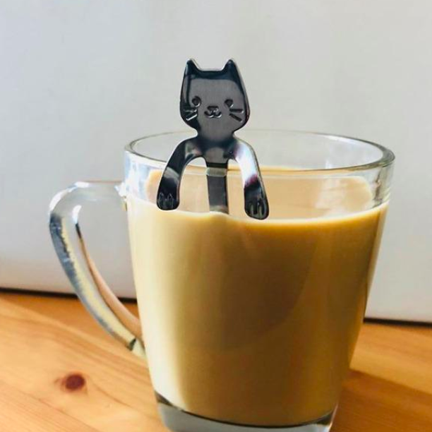 A cat-shaped stirring spoon delicately positioned against a cup of coffee.