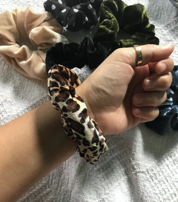 A reviewer wearing a leopard print scrunchie on their wrist, with several others visible in the background.