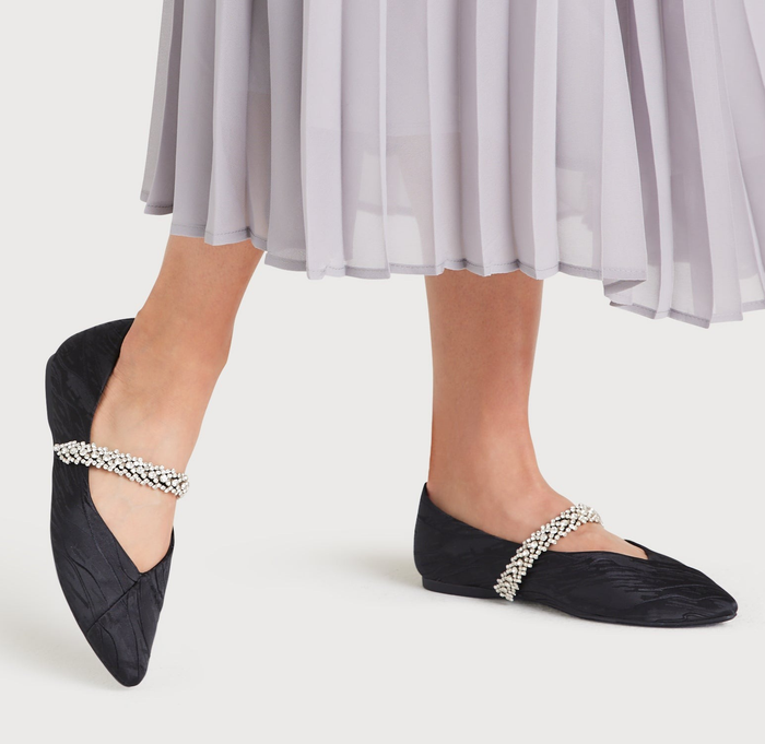A model showcasing black flats adorned with a crystal band across the top.