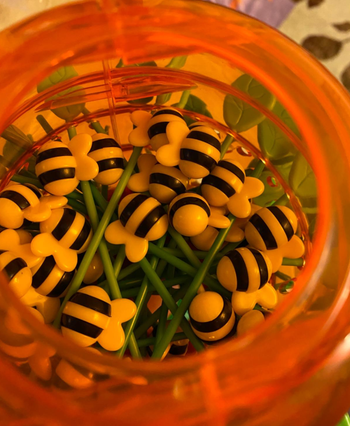 A jar filled with bee-themed toys, featuring yellow and black stripes, placed on green stems.