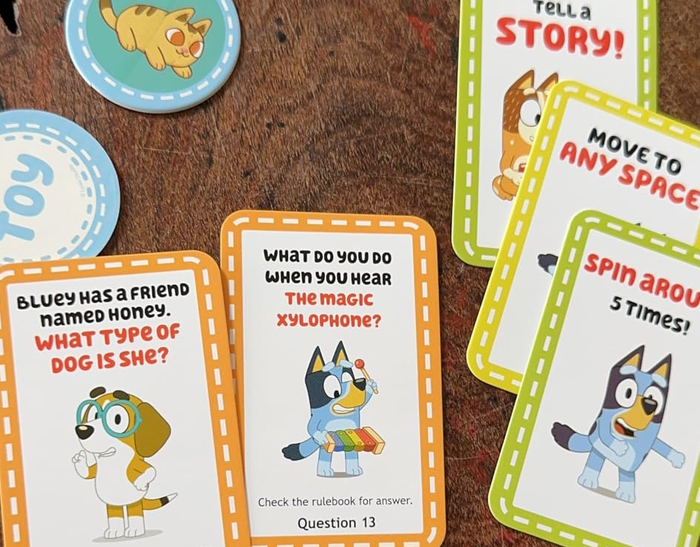 A variety of Bluey-themed game cards are laid out on a table, featuring questions and instructions for players.