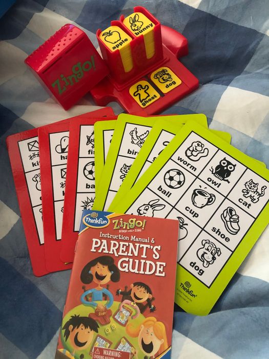 The Zingo game set includes a red and yellow Zingo! dispenser, along with red and green cards adorned with various images.