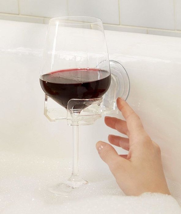 A clear holder attached to the side of the bathtub, with a stemmed wine glass inside.