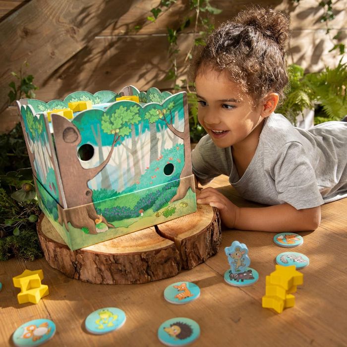 A young child enjoys playing with a forest-themed DIY toy box surrounded by nature-inspired game pieces, offering a world of imaginative play.