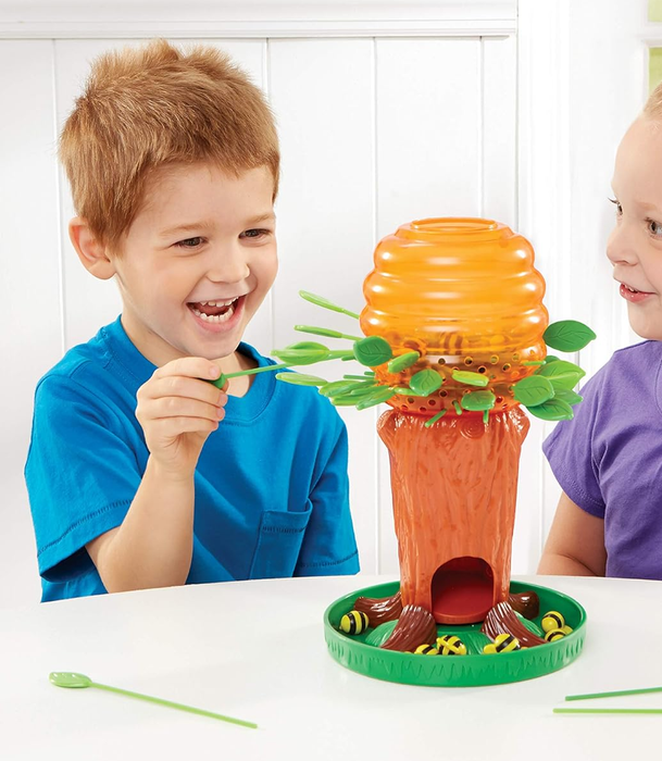 Two young children, a boy in a blue shirt and a girl in a purple shirt, are enjoying a tree-themed game, placing leaves into different slots on the tree.