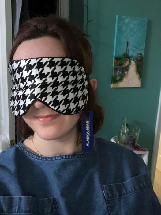 A reviewer wearing a stylish, oversized eye mask with a houndstooth pattern.