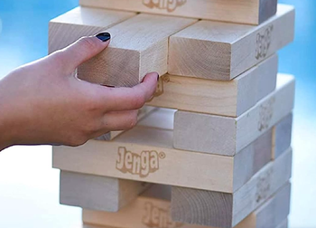 A close-up view of a hand pulling a block from a Jenga tower.