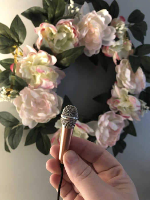 A hand holding a tiny microphone in front of a festive wreath