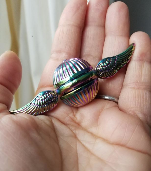 A reviewer holding the rainbow-colored toy resembling a Flying Snitch with wings extending from both sides.