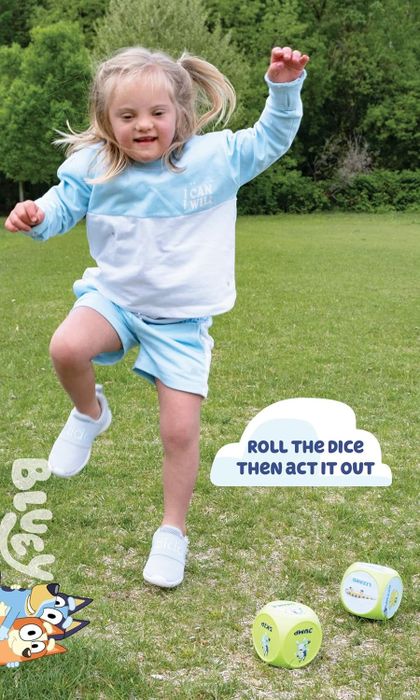A child is happily playing outside in a grassy field, dressed in a sweatshirt and shorts. Two large dice guide them through different actions.
