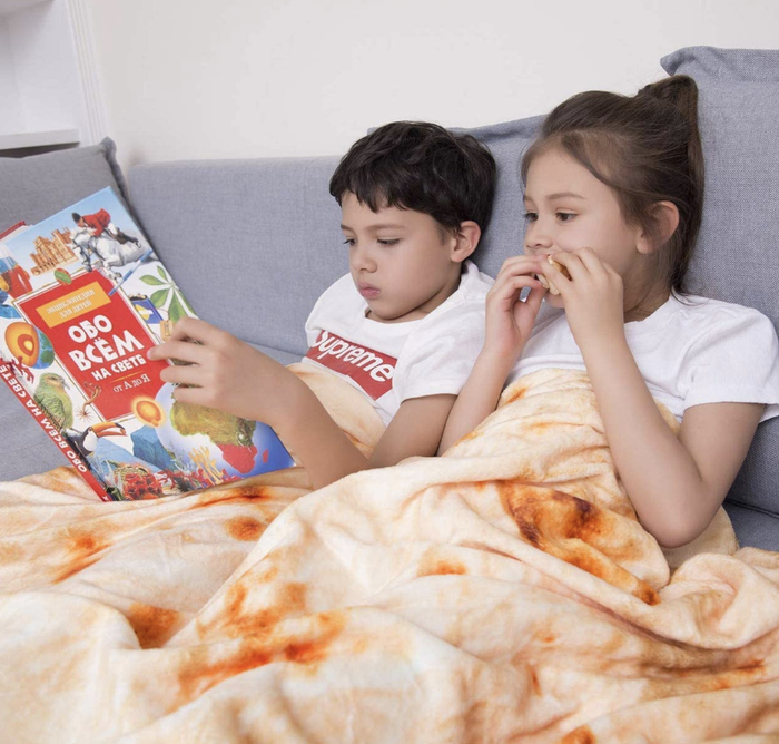 Two children snuggled under a blanket, reading together.