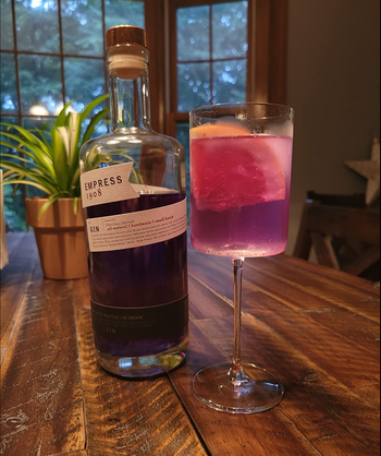 A clear, cylinder-shaped stemmed wine glass filled with pink gin.