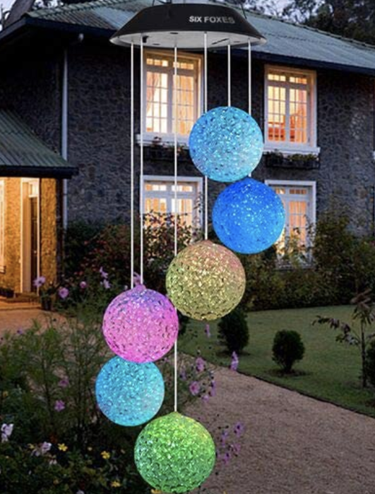 A vibrant solar wind chime hanging on a tree outside someone's house.
