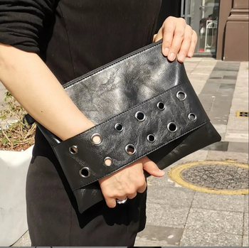 A model showcasing a black envelope clutch held by a leather strap.
