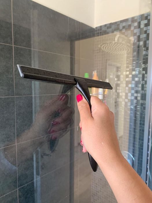 A reviewer uses a squeegee to wipe down the glass walls of the shower, leaving them spotless.