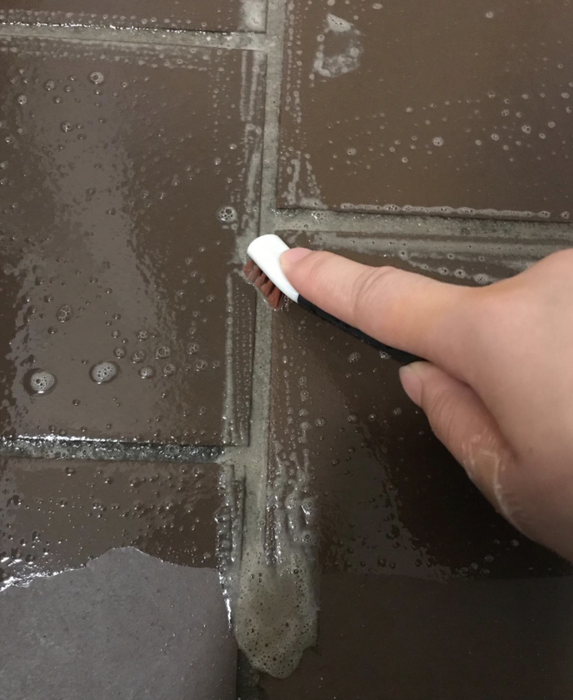 A reviewer using the OXO brush to clean between tiles