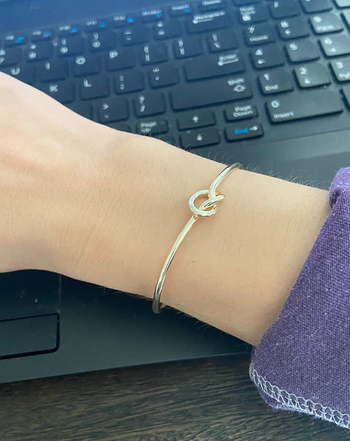 A reviewer showcasing a delicate gold band with a subtle knot design at the top, worn on their wrist.