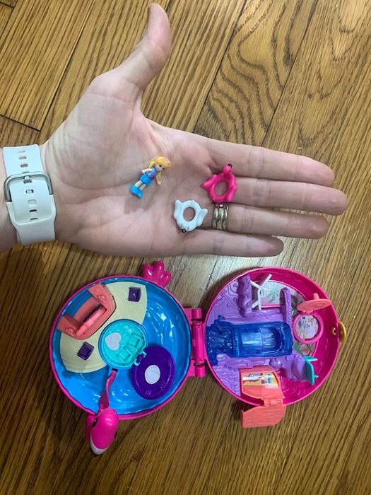 A reviewer holds the small pieces that come with the playset in one hand, while the compact case is placed on the floor.