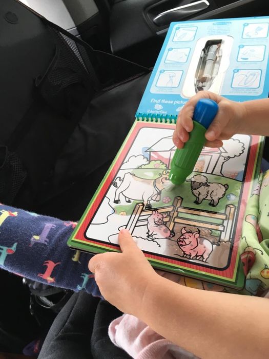 A child coloring with the water pen on the activity pad while in a car.