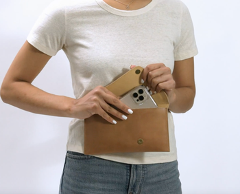 A woman placing her iPhone into a beige envelope clutch.